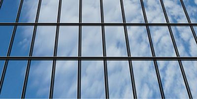 Ein Hochhaus mit einer Glasfront, in der sich Wolken vom Himmel spiegeln.