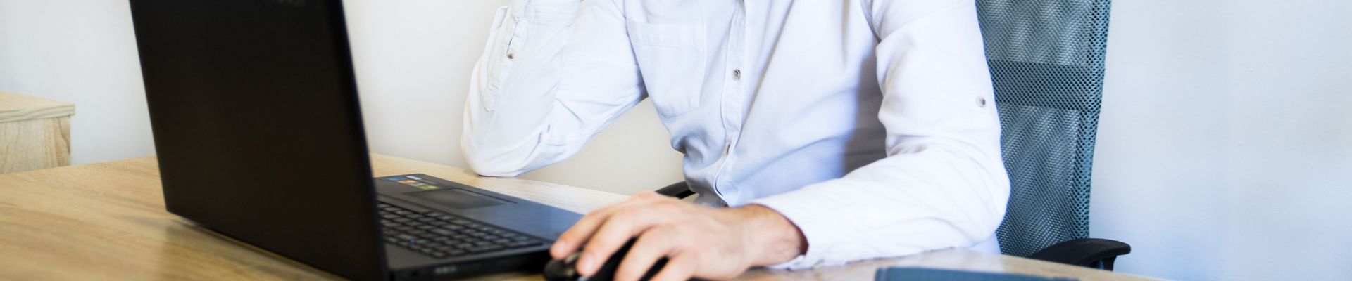 Ein Mann sitzt an einem Schreibtisch, telefoniert und arbeitet an seinem Laptop.