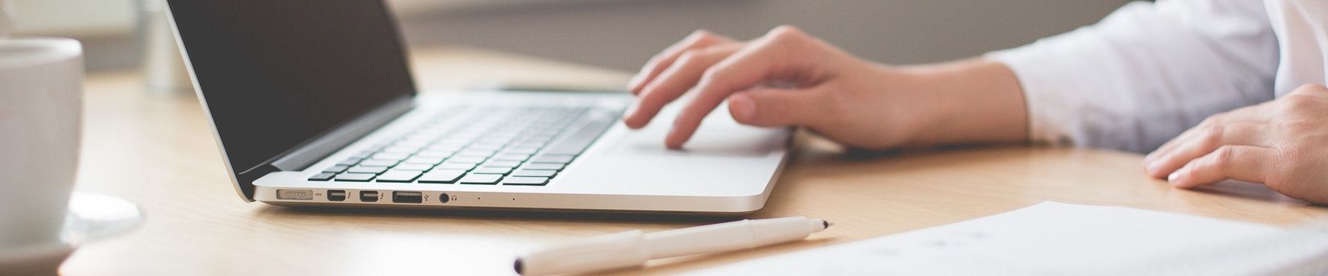 Eine Frau sitzt an einem Tisch und arbeitet an ihrem Laptop.