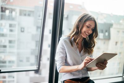 Eine Frau steht vor dem Fenster und arbeitet an einem Tablet
